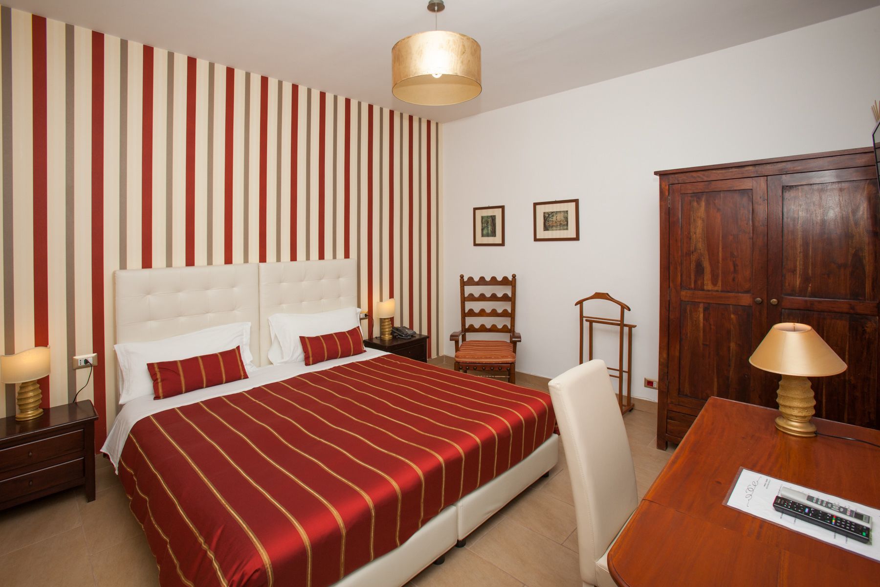 A hotel room with a large bed, a wooden wardrobe, a desk with a lamp, and a striped wall.