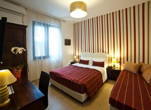 A hotel room with a large bed, a smaller bed, a desk with a lamp, a chair, and a window with curtains.