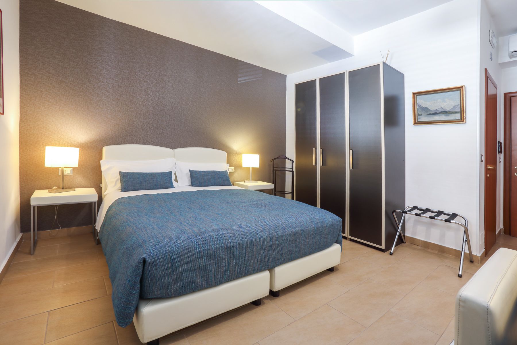 Una camera da letto con un letto, due comodini con lampade, un armadio, un portascopevoli e un quadro appeso al muro.