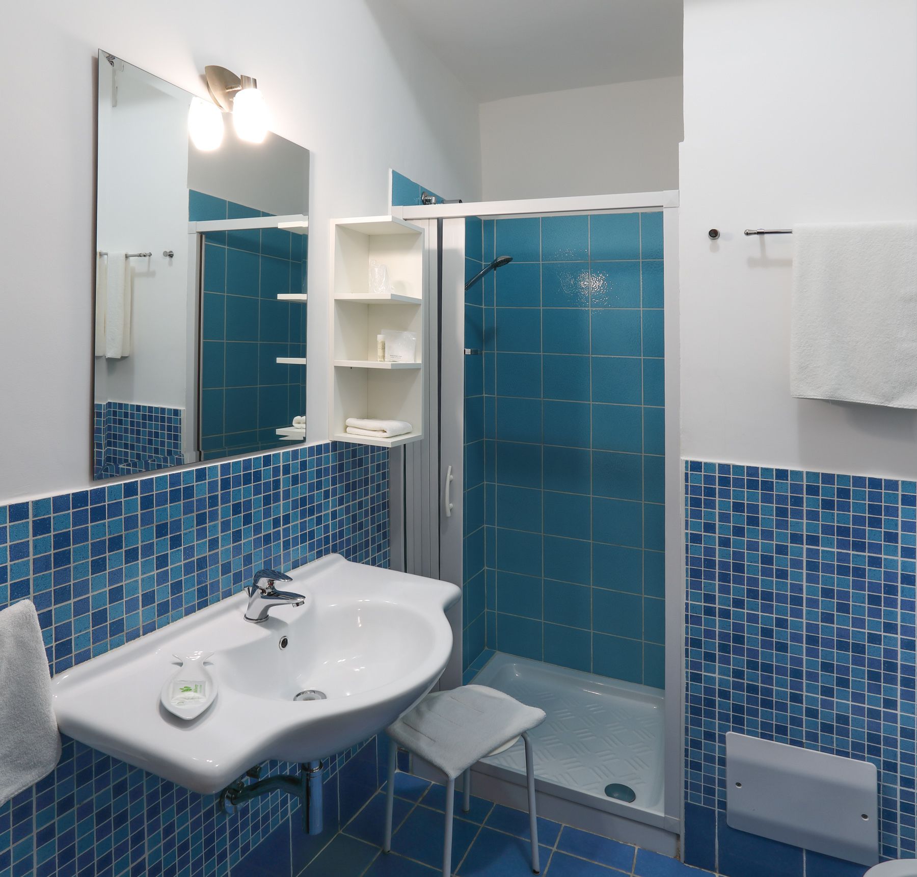 A bathroom with a white sink, a mirror, a shower with blue tiles, and a white towel hanging on the wall.
