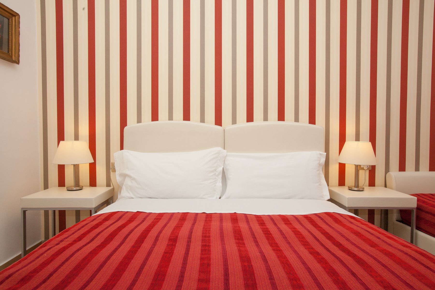 A neatly made bed with white linens, two bedside lamps, and a red-striped blanket.