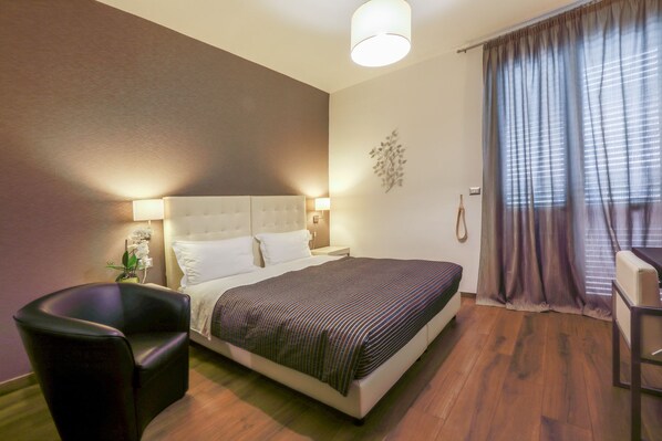 A hotel room with a bed, bedside lamps, a chair, a desk, and a window with curtains.