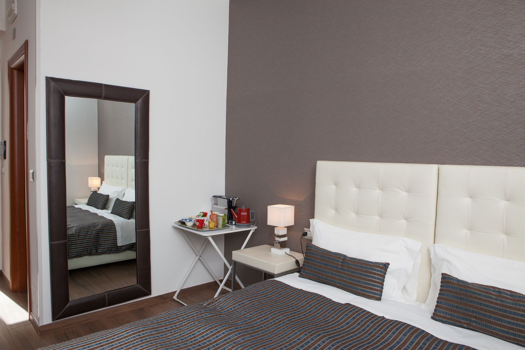 Ein Hotelzimmer mit Bett, Nachttisch, Spiegel und einem kleinen Tisch mit Lampe und Kaffeemaschine.