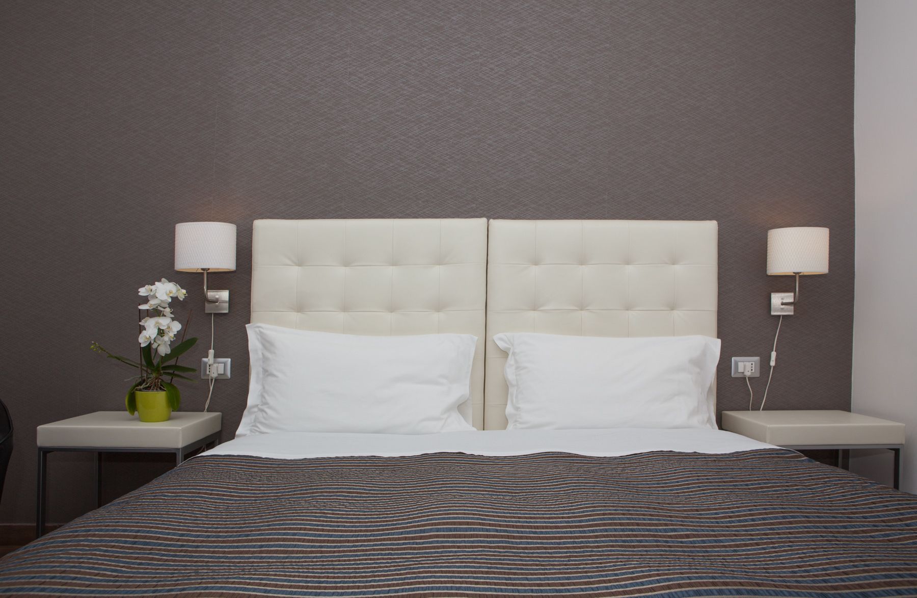 A double bed with a striped bedspread, two white pillows, a tufted headboard, and two bedside lamps.