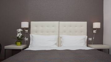 Una cama doble con una colcha a rayas, dos almohadas blancas, un cabecero capitonado y dos lámparas de noche.