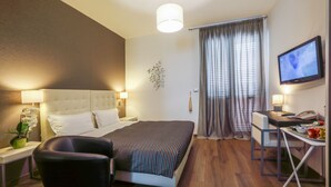 Una habitación de hotel con cama, escritorio, silla, televisor y ventana con cortinas.
