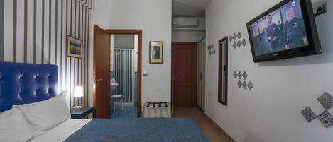 Habitación de hotel con una cama grande, televisión y baño visible a través de una puerta abierta.