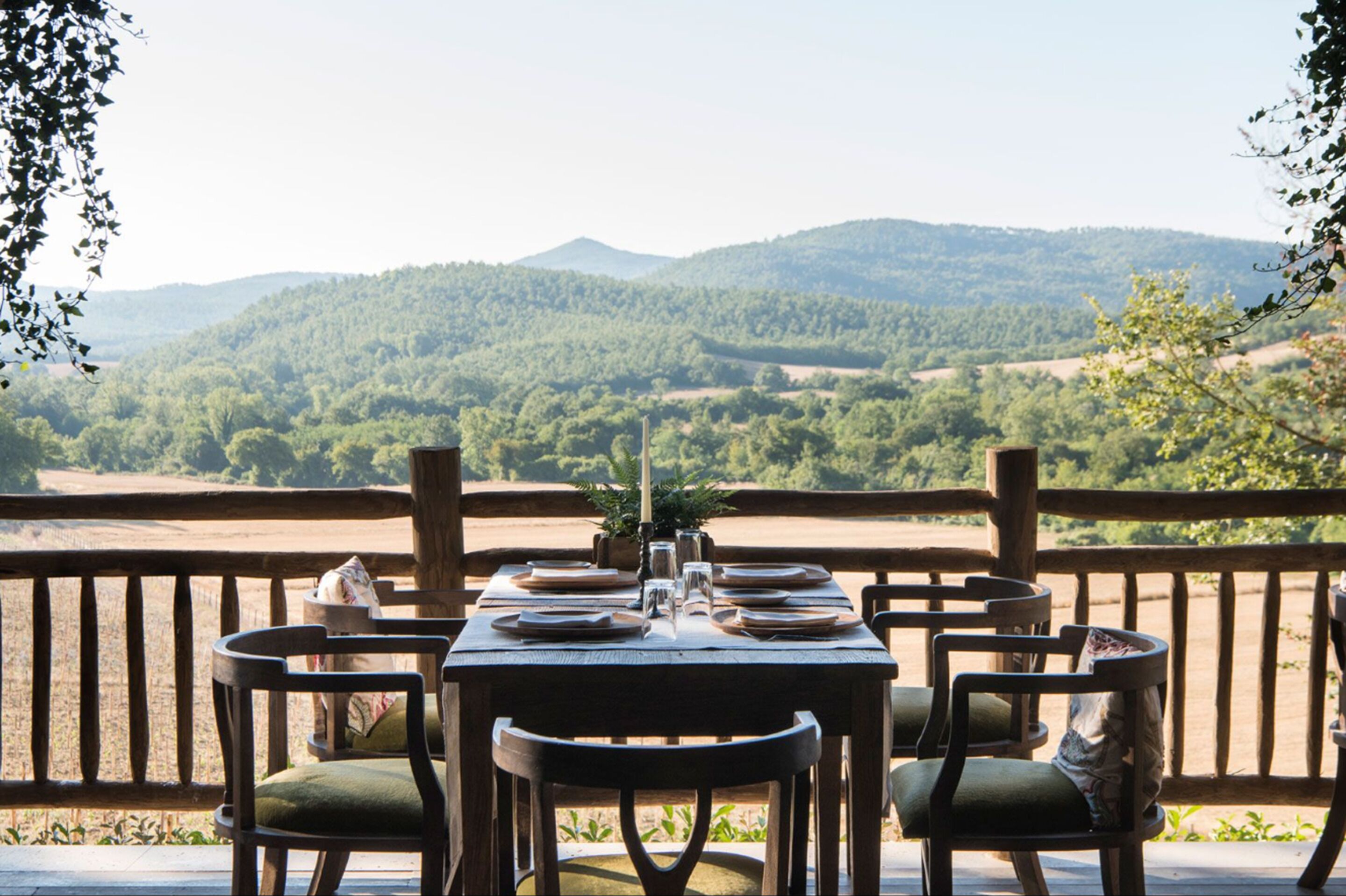 A wooden table set for dining with chairs, overlooking a mountainous landscape.