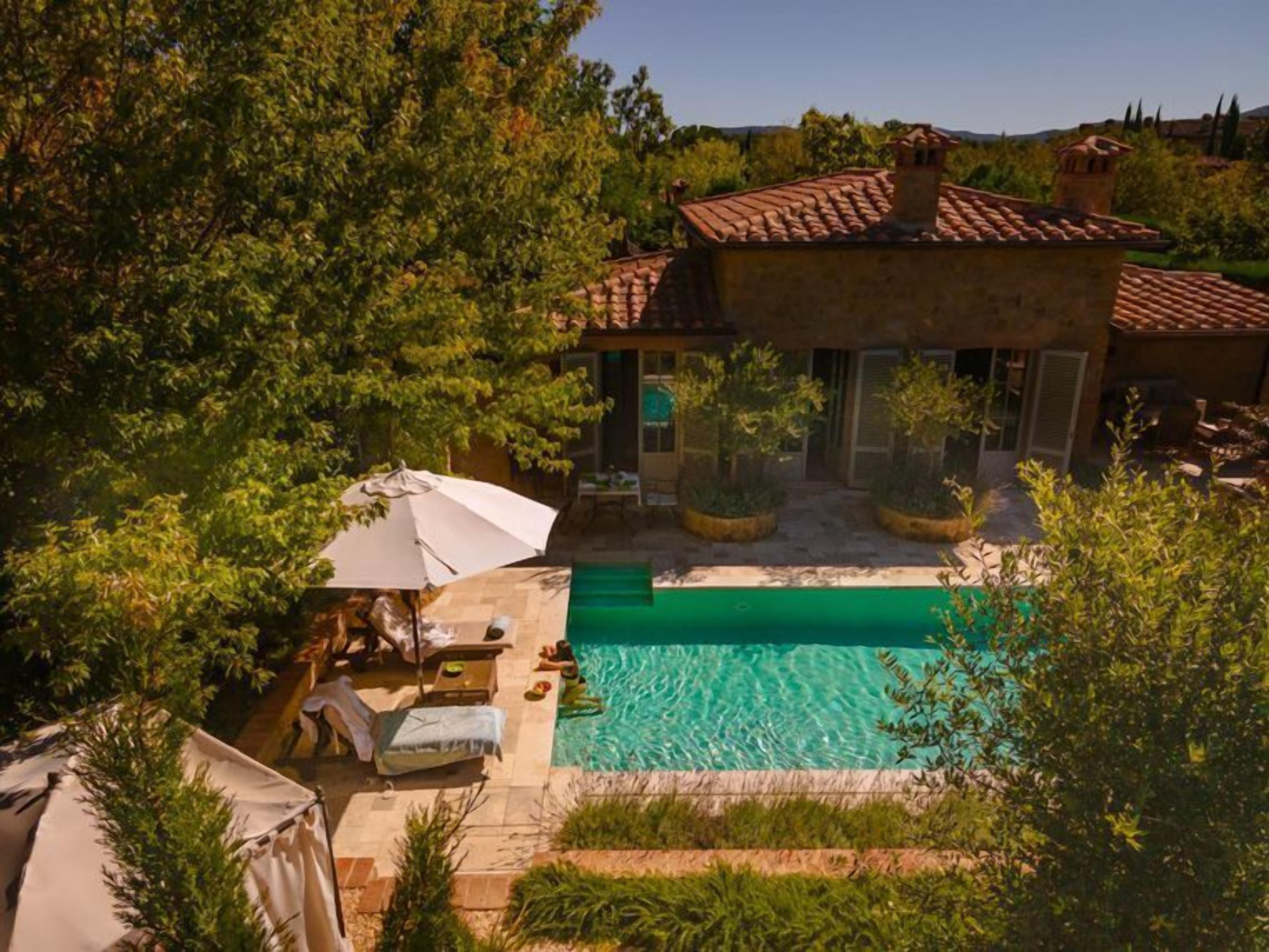 A pool area with a tiled deck, lounge chairs, and umbrellas.