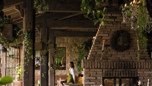 Un coin repas rustique avec des murs en briques, des plantes suspendues et des tables éclairées à la bougie.