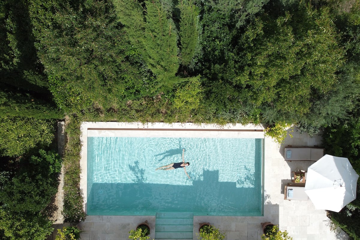 An aerial view of a rectangular swimming pool surrounded by lush greenery, with a person swimming.