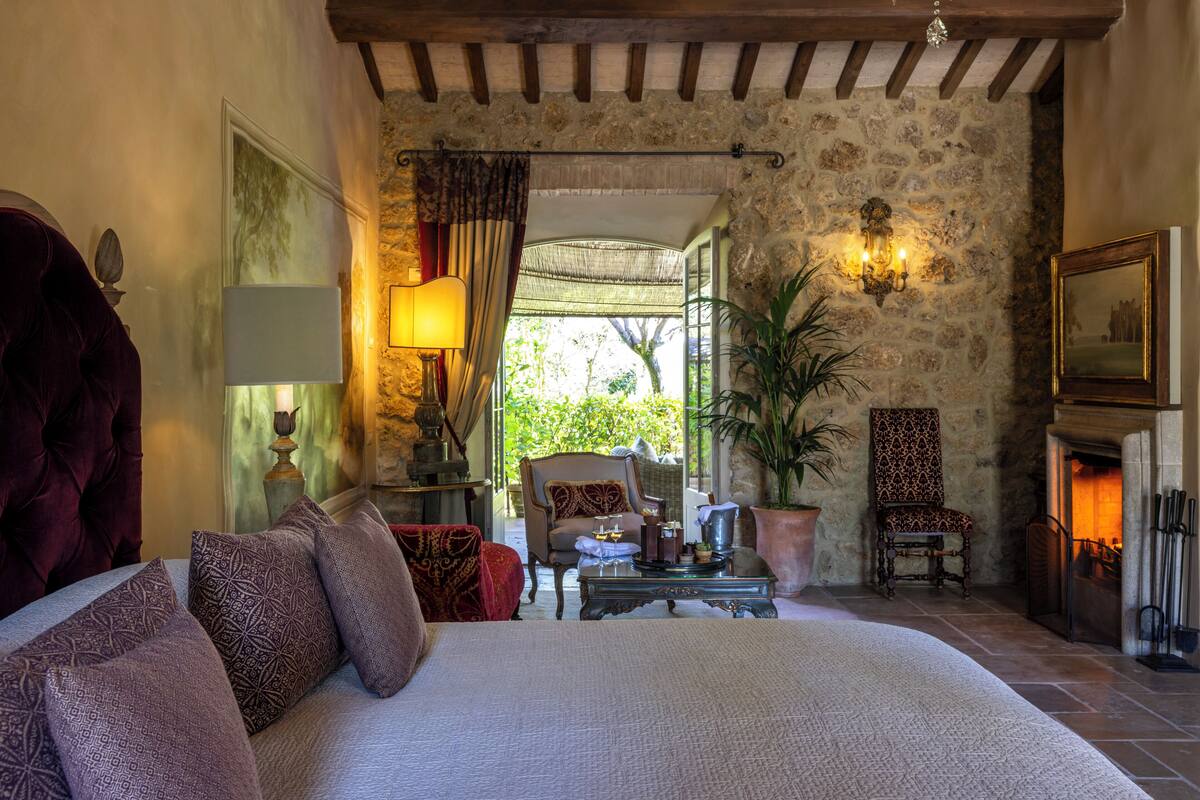A spacious bedroom with a large bed, a sitting area with a fireplace, and a stone wall.