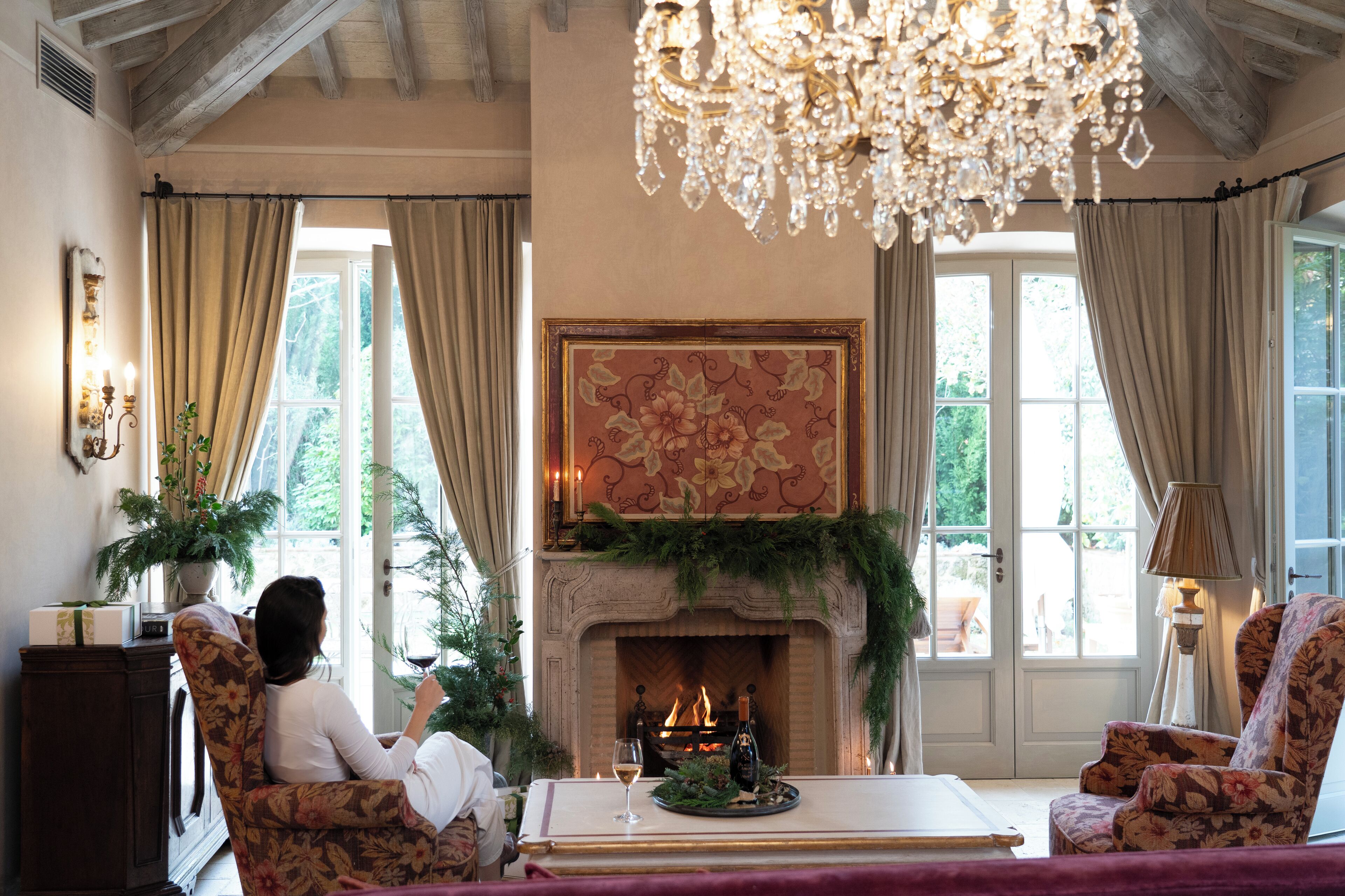 A cozy living room with a fireplace, floral armchairs, and a chandelier.
