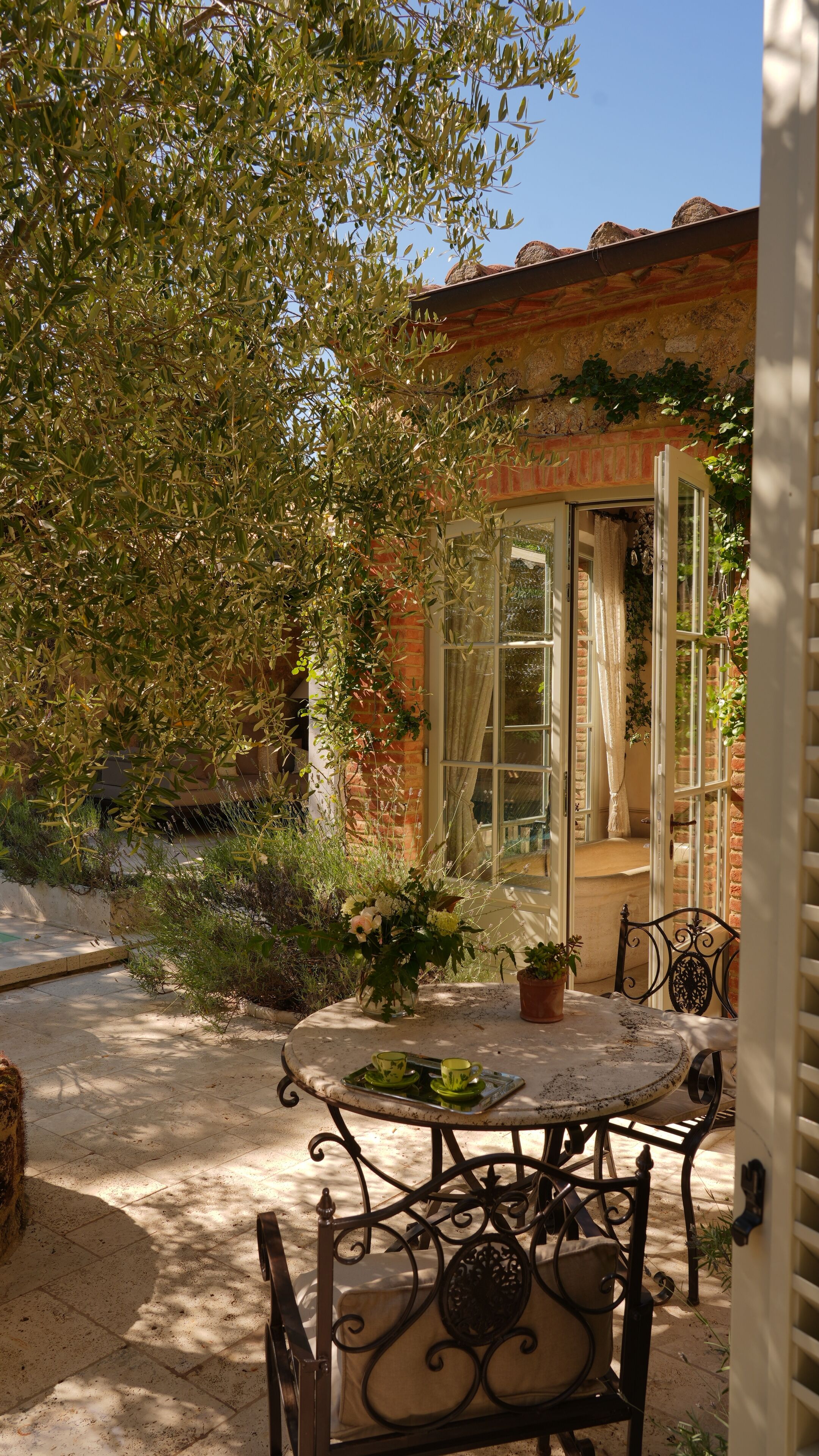 Un patio al aire libre con una mesa redonda y sillas, una planta en maceta y una puerta de vidrio que da a una habitación.