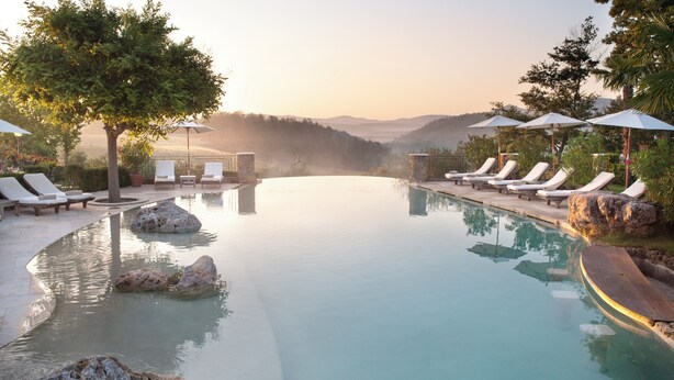 A serene infinity pool with lounge chairs and umbrellas, surrounded by natural scenery and a clear view of distant mountains. - Borgo Santo Pietro (Chiusdino)