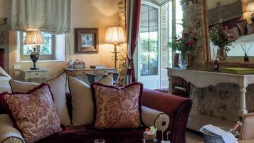 A cozy room with a wooden ceiling, a plush red sofa, a glass coffee table with wine glasses, and a stone wall with a mirror.
