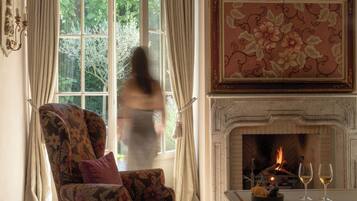A room with a large window, a fireplace, and a floral armchair.