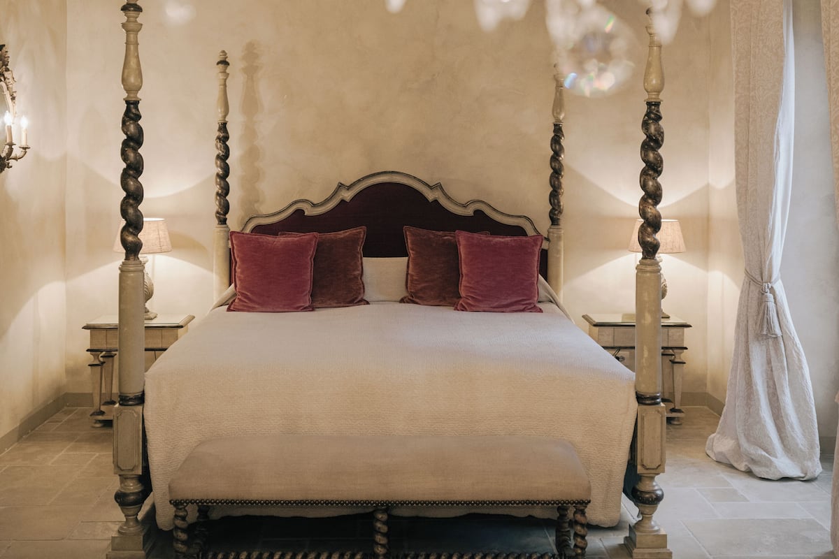 A four-poster bed with a dark wooden frame and a white bedspread, flanked by two bedside tables with lamps.