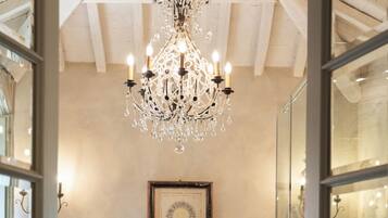 A bathtub in a room with a chandelier, framed artwork on the wall, and a glass door leading to another room.