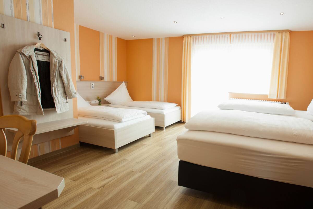 Ein Hotelzimmer mit zwei Einzelbetten, einer Schlafcouch, einem Holztisch und einem Stuhl.