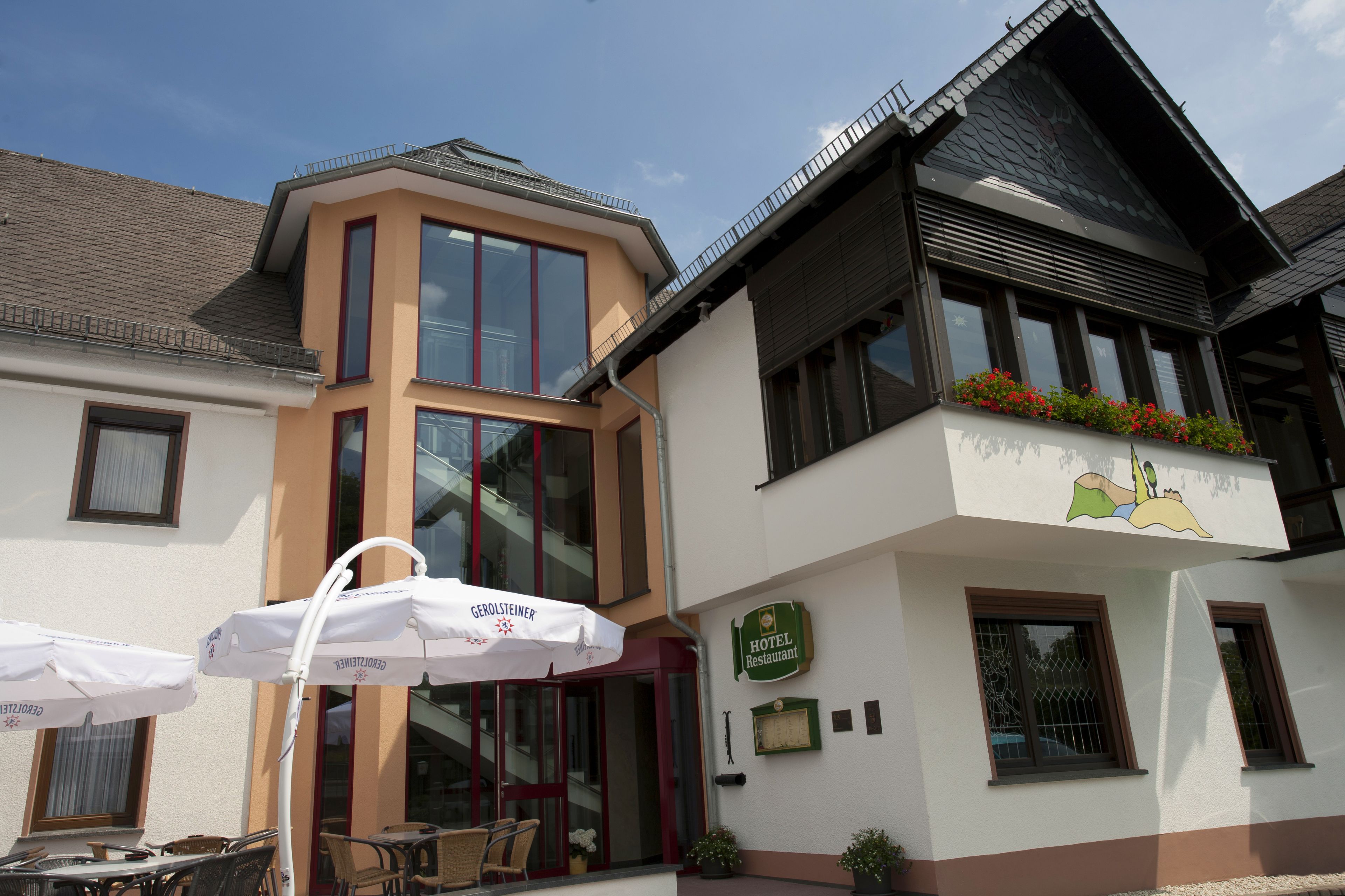 Een hotel met een modern design, met grote ramen, terras met parasols en een bord dat aangeeft dat het een hotelrestaurant is.