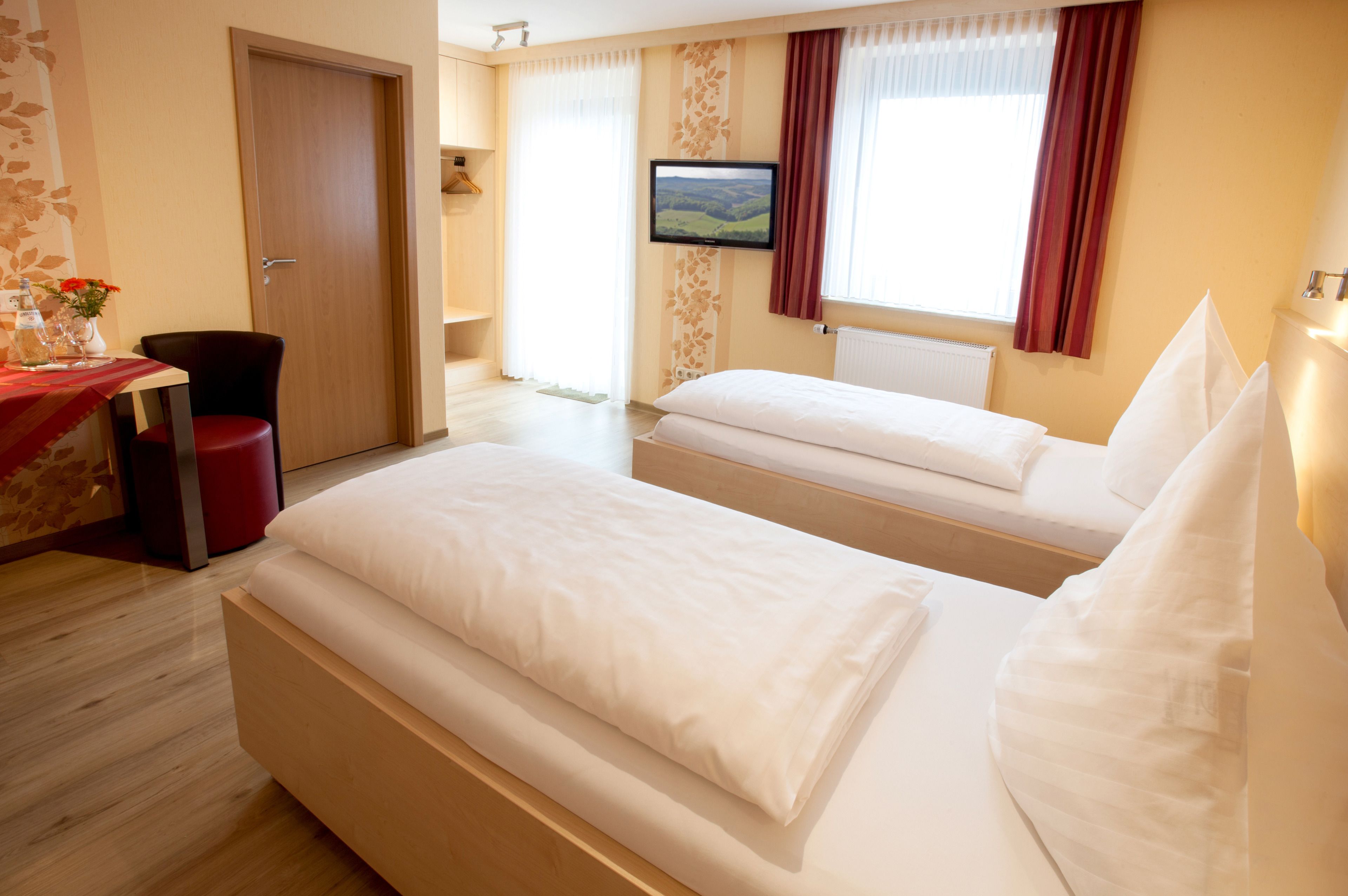 Hotelkamer met twee bedden, een televisie, een bureau met stoel en een raam met gordijnen.