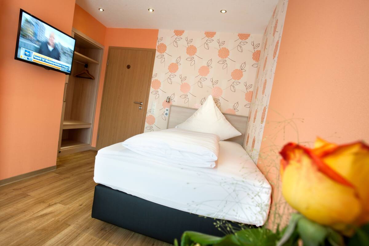 Ein Hotelzimmer mit einem Bett, einem an der Wand befestigten Fernseher und einer Holztür.