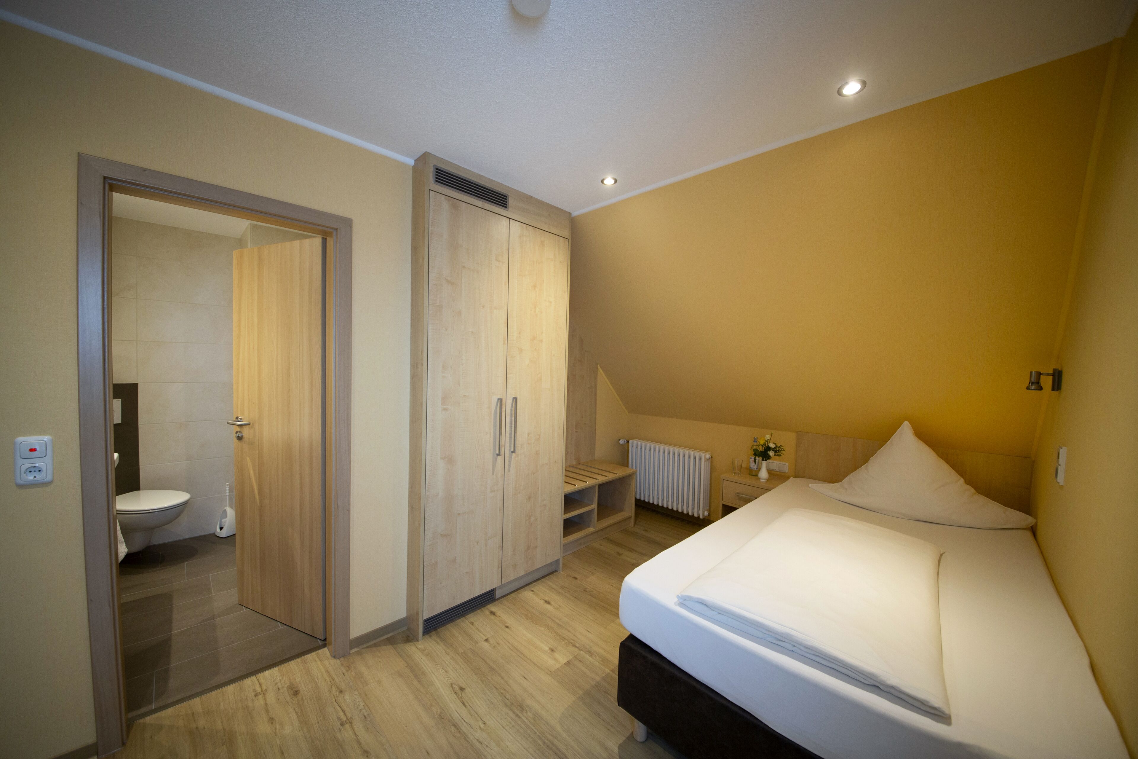 A bedroom with a bed, a wooden wardrobe, a radiator, and a bathroom with a toilet.