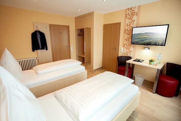 Habitación de hotel con dos camas, un escritorio, un televisor y un armario.