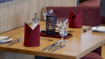A restaurant setting with a wooden table set for two, including cutlery, glasses, and a candle holder.