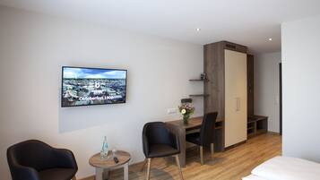 Ein modernes Hotelzimmer mit Holzboden, einem Bett, einem Schreibtisch mit Stuhl, einem an der Wand befestigten Fernseher und einem Kleiderschrank.
