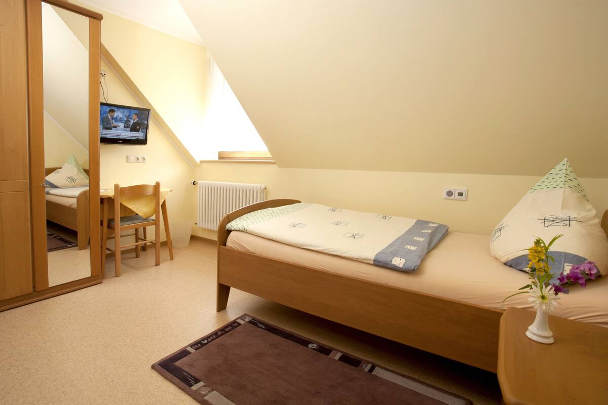 Ein Schlafzimmer mit einem Einzelbett, einem Sessel, einem kleinen Tisch, einem an der Wand montierten Fernseher und einer Heizung.