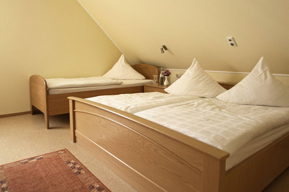 Ein Schlafzimmer mit einem Bett, einem Einzelbett und einem Nachttisch mit einer Vase.
