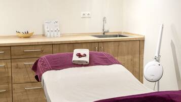 A hotel room with a bed, a small window, a sink, a mirror, and a bedside table with toiletries.