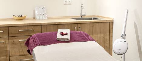 A hotel room with a bed, a small window, a sink, a mirror, and a bedside table with toiletries.