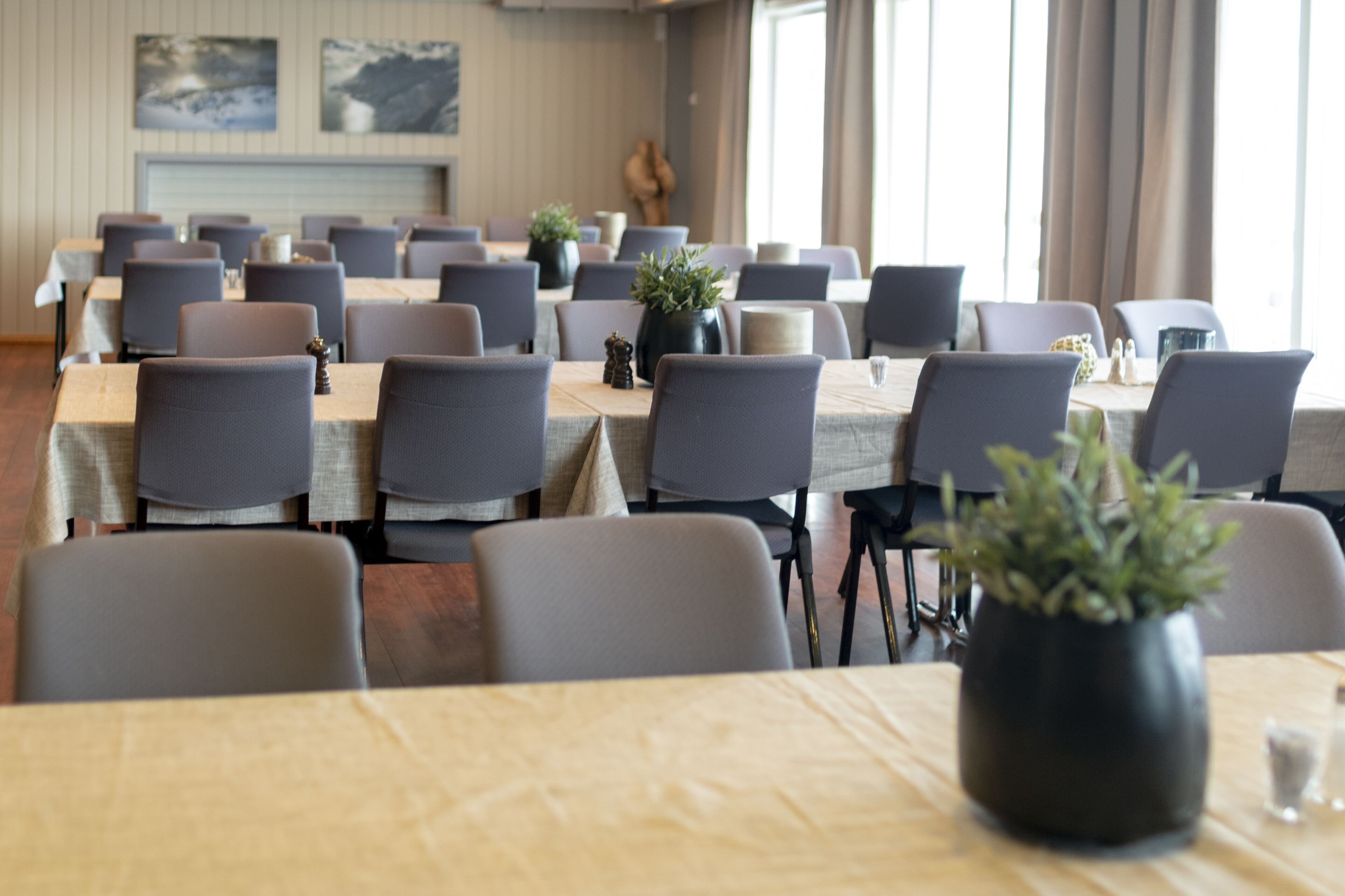 Ein Konferenzraum mit mehreren Tischen, Stühlen, Zimmerpflanzen und Kunstwerken an den Wänden.