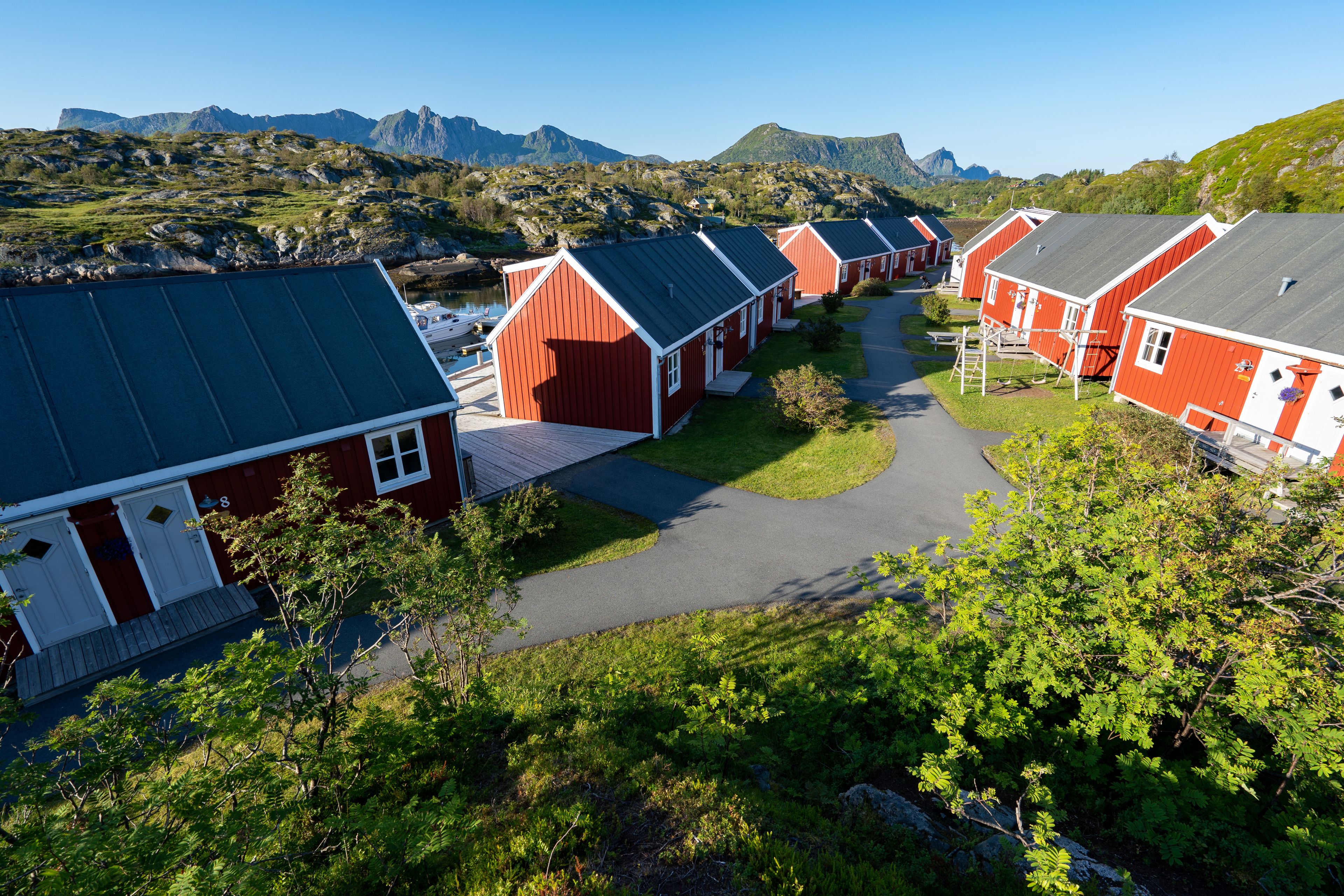 A row of red cabins with sloped roofs, arranged along a path with a mountain backdrop.