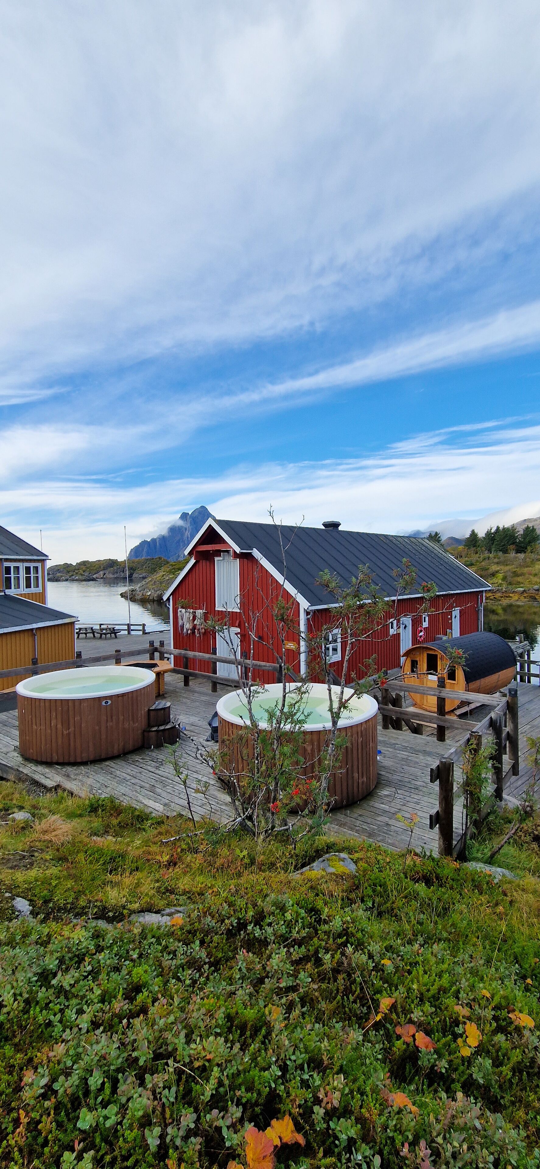 A red wooden building with a dock, hot tubs, and a wooden deck.