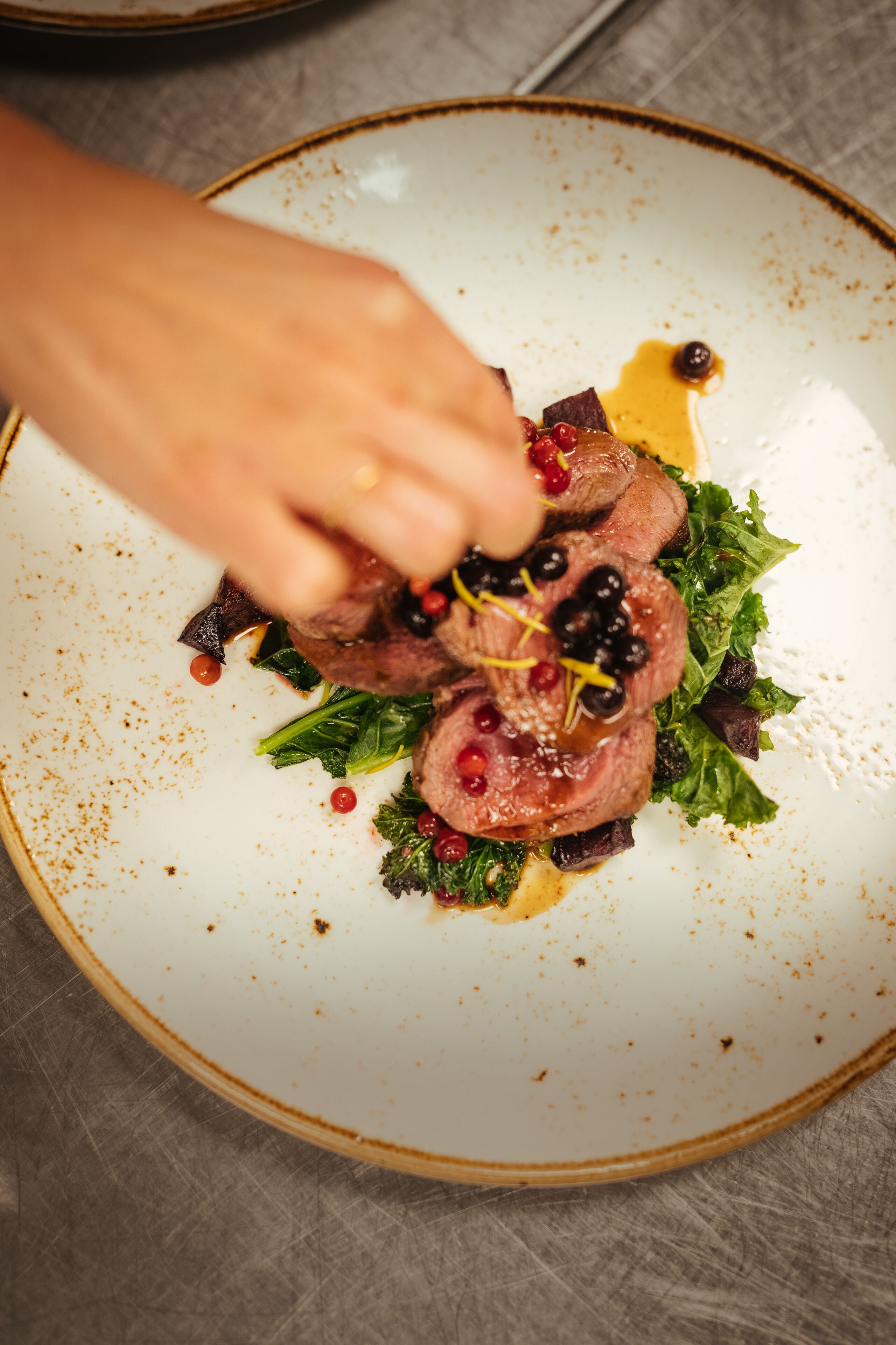 A plate with sliced meat, greens, and berries.