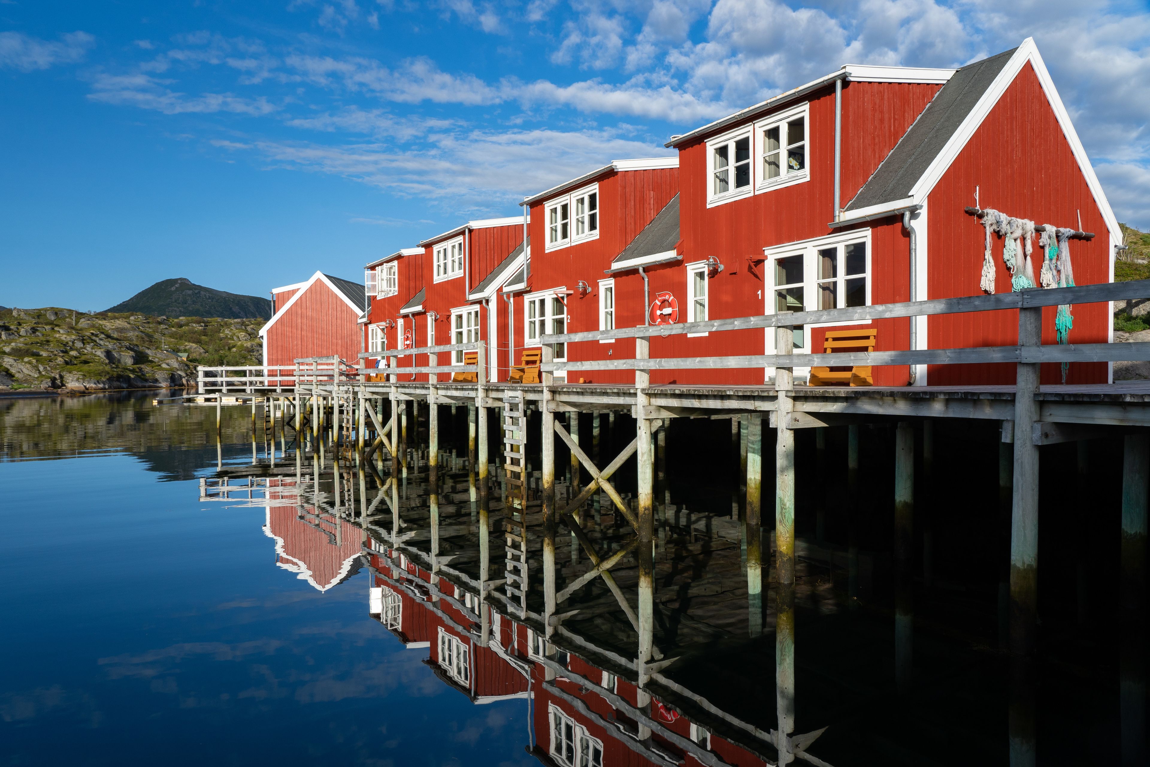 A row of red buildings with white trim, connected by a wooden walkway over water.