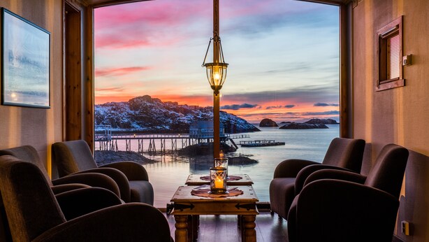 Un comedor con vistas a un atardecer sobre el agua, con una mesa, una vela y varias sillas tapizadas.