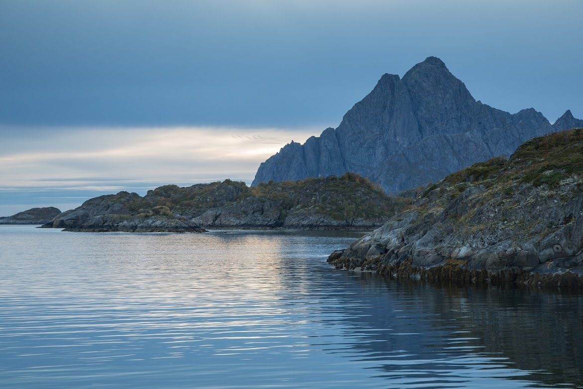 A calm body of water reflecting a rugged mountain landscape.
