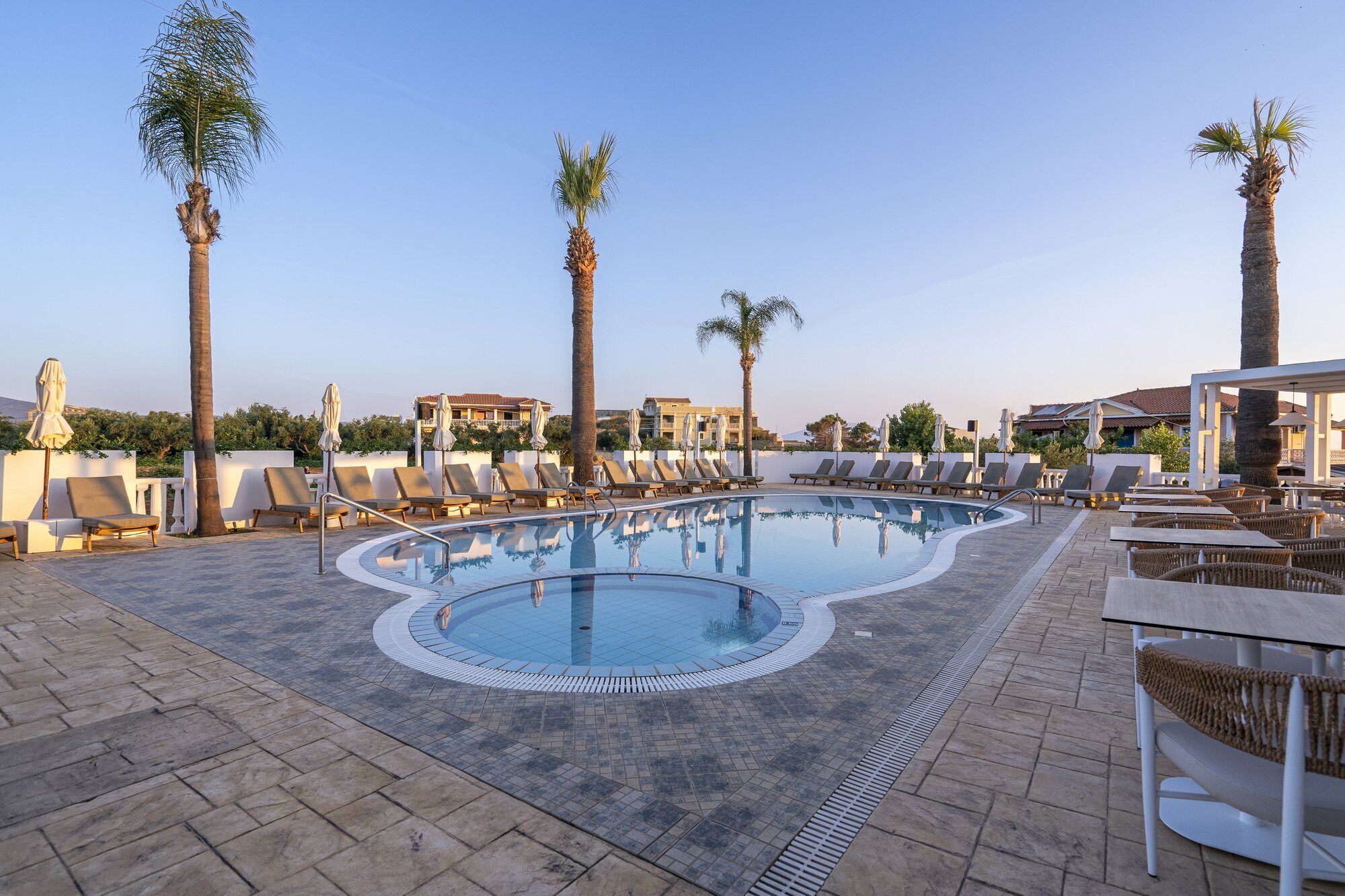 Un área de piscina con sillones de descanso y palmeras.