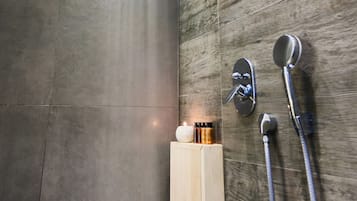 A modern shower with a rain showerhead, a handheld showerhead, and a soap dispenser on a wooden panel wall.