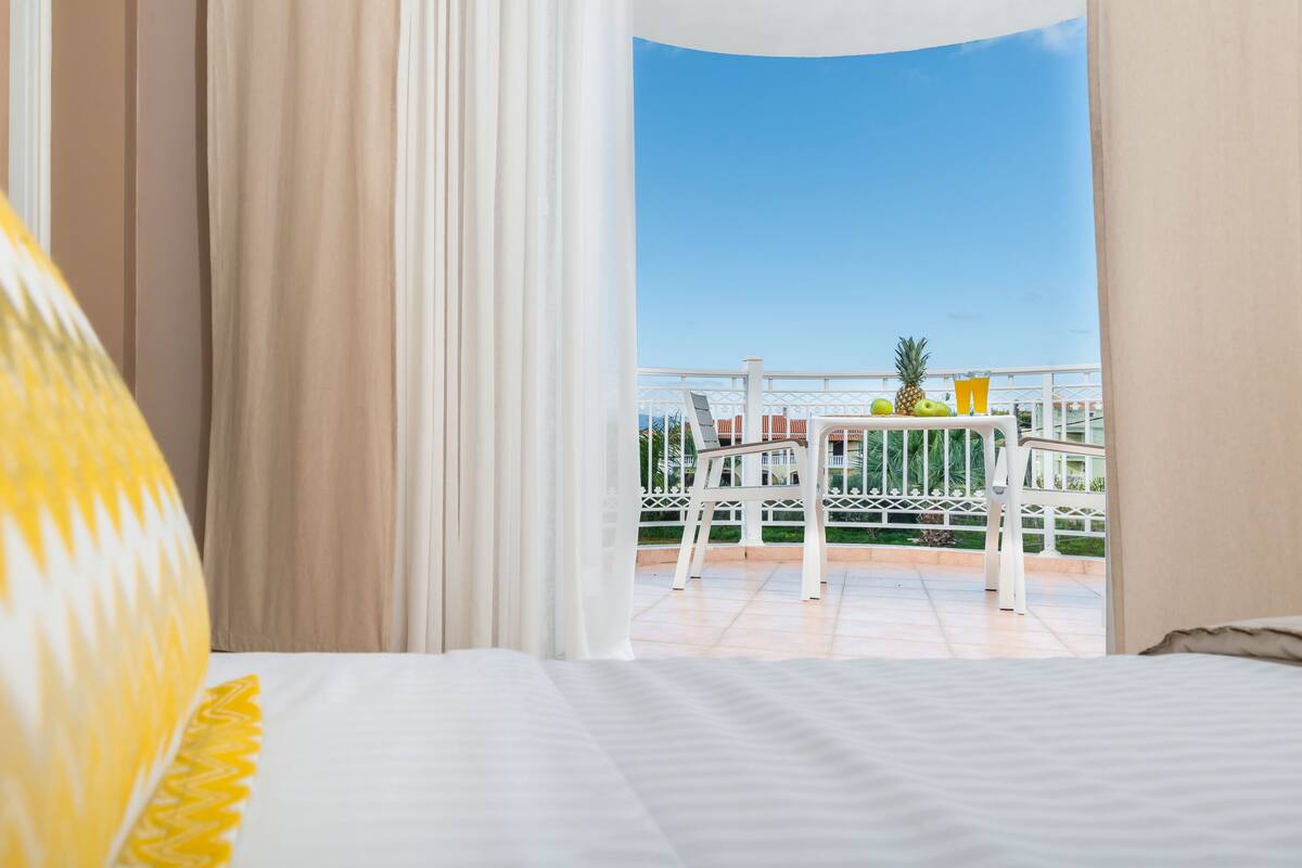 Una habitación de hotel con cama, cortinas y un balcón con mesa y sillas.