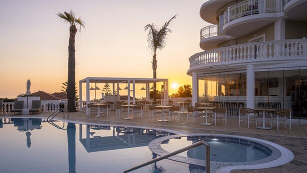 A pool area with lounge chairs and umbrellas, a covered seating area, and a building with balconies. - Arkadia Luxury Hotel Apartments (Zakynthos)