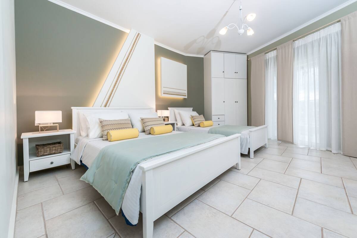 Un dormitorio con una cama grande, mesitas de noche, un armario y una ventana con cortinas.