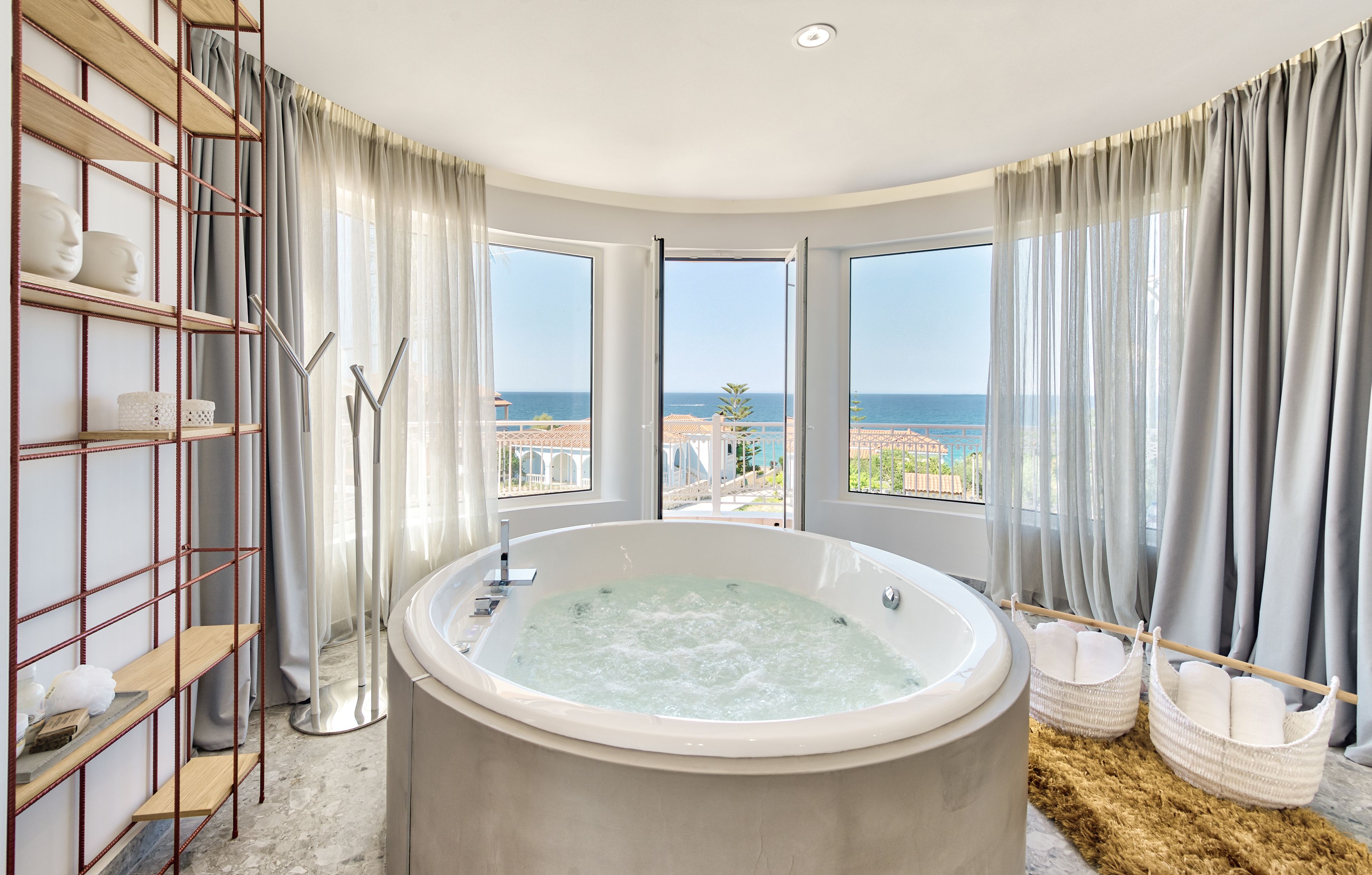 Ein modernes Badezimmer mit einer großen Badewanne, einem Holzregal und Meerblick.