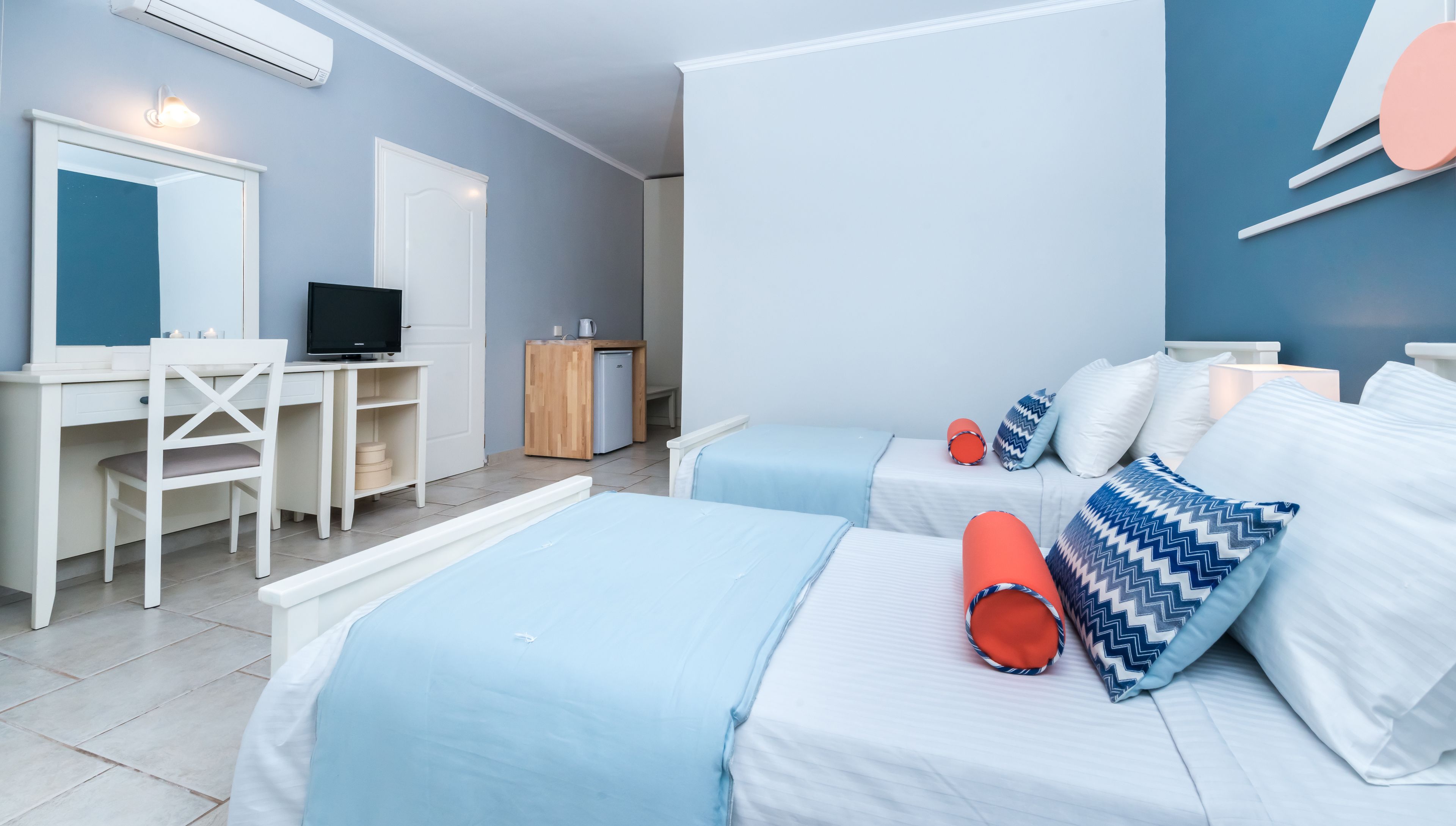 Een slaapkamer met twee bedden, een bureau, een televisie en een kleine kitchenette.