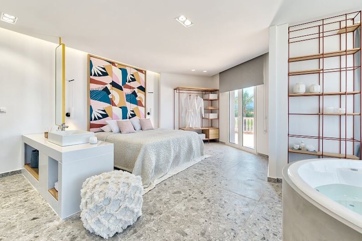Une chambre moderne avec un grand lit, une coiffeuse blanche, une baignoire et une grande fenêtre.